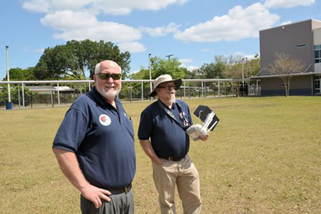 Patrick Phillips (right) holds a drone controller as he demonstrates a flight in the school yard, while his colleague James Mazurak (left) watches.