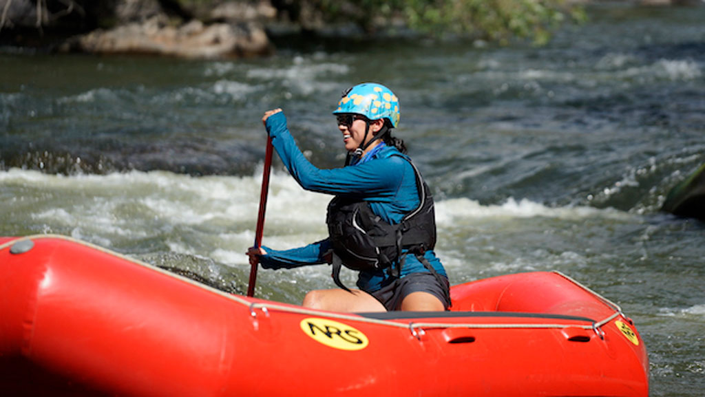 Photo of Sophia Garcia padding a raft in river rapids