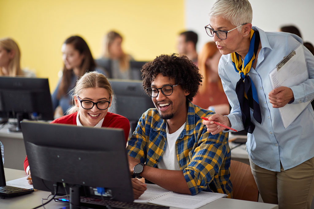 Photo of instructor consulting with students as they perform tasks on theirs computer