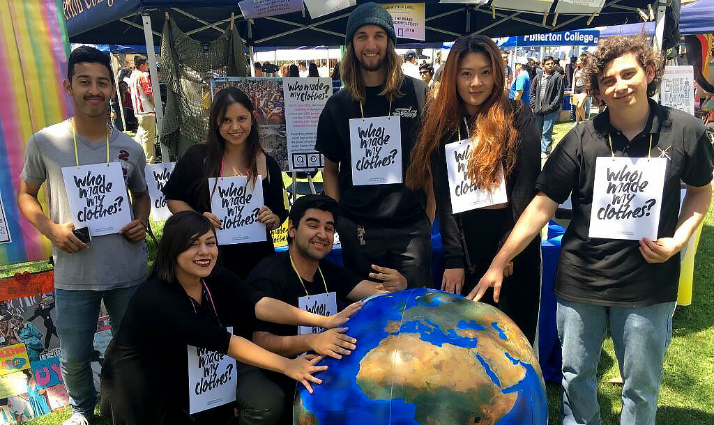 Photo of Fullerton College geography students attending a fair pose with a large globe and hold signs saying "Who made my clothes?". Courtesy Fullerton College