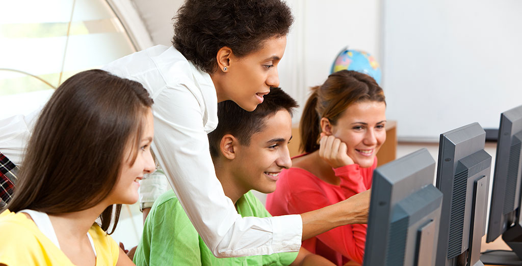 Teacher pointing at computer monitor with three high school students looking on