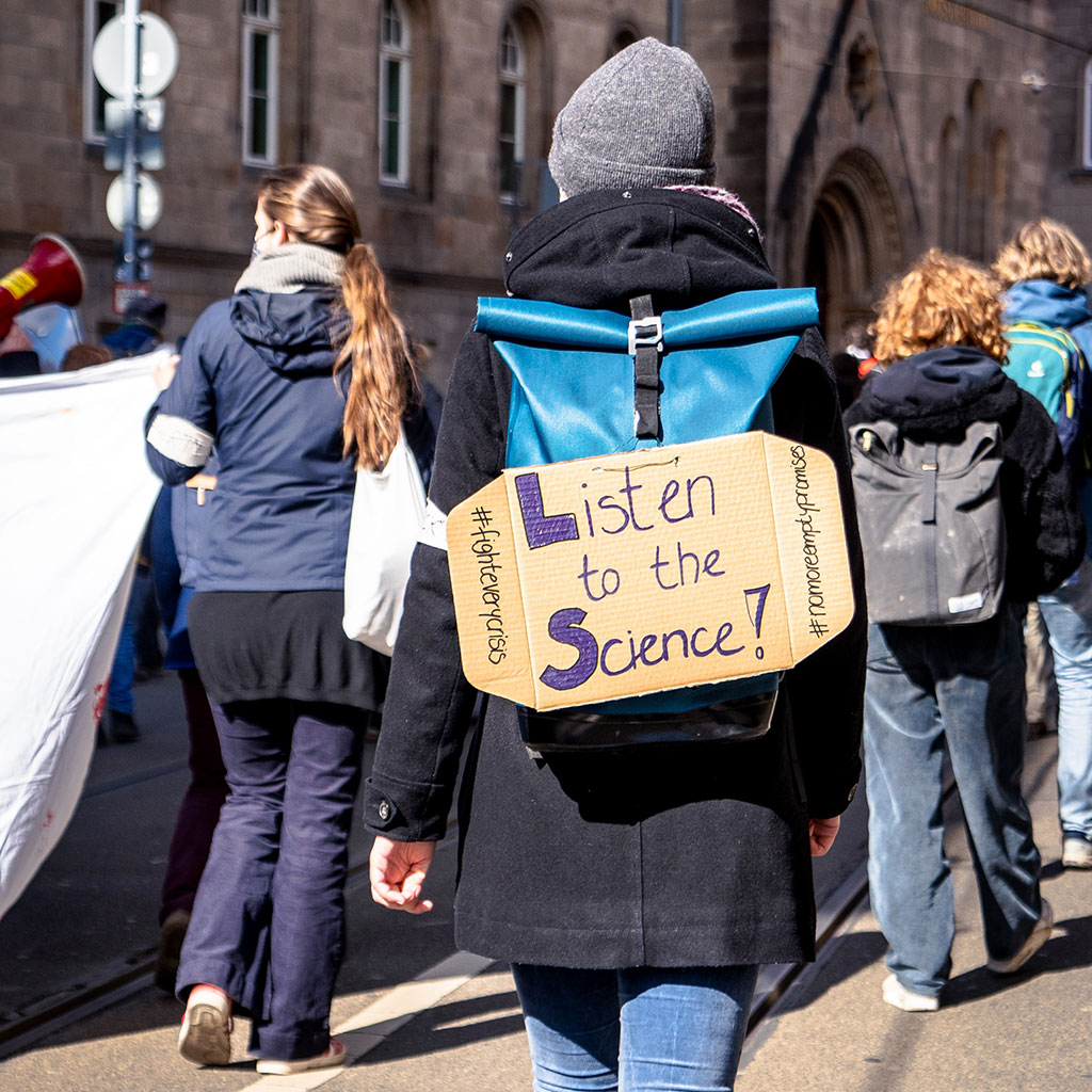 Protesters march for climate change with sign, saying "Listen to the Science" Credit: Mika Baumeister for Unsplash