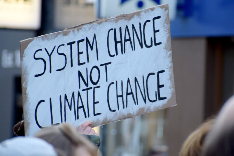 Sign with message, "System change not Climate Change"; Photo by Ma Ti, Unsplash