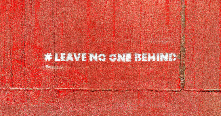 Message painted on wall that says "asterisk" Leave no one behind; photo by Etienne Girardet for Unsplash