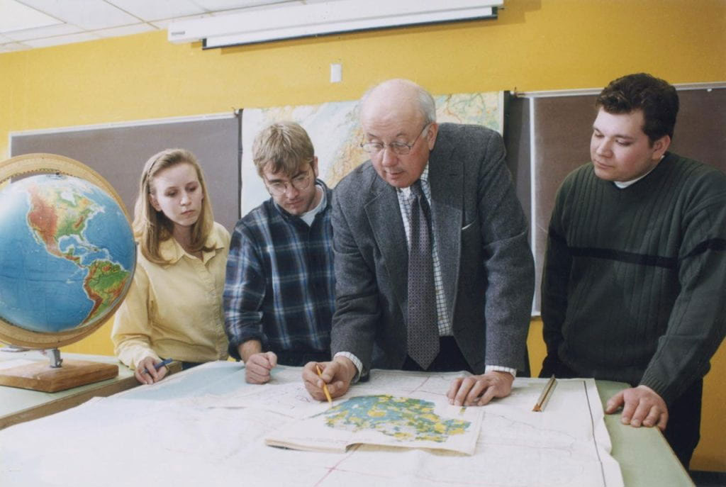 Photo of William Laatsch pointing to a desk map with students looking on