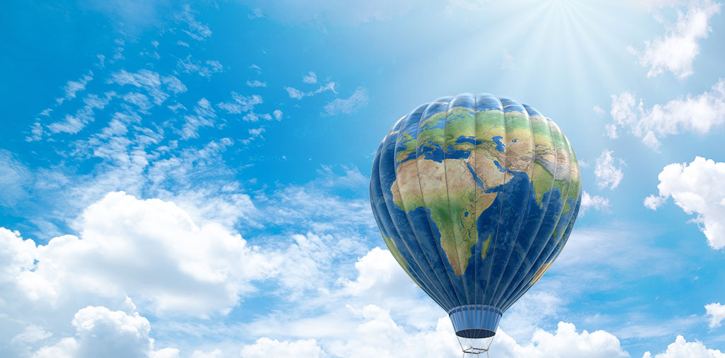 Hot air balloon with the image of the globe floats through a sunny sky with cloud formations