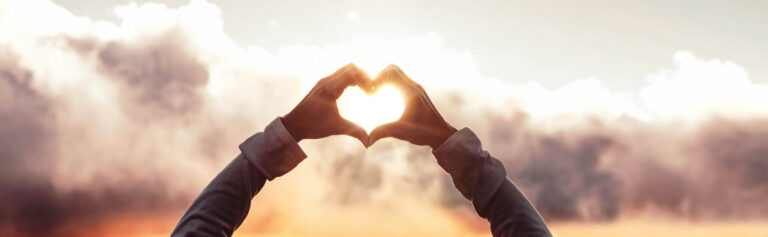 Person holding their hands in the shape of a heart with sunlight in background