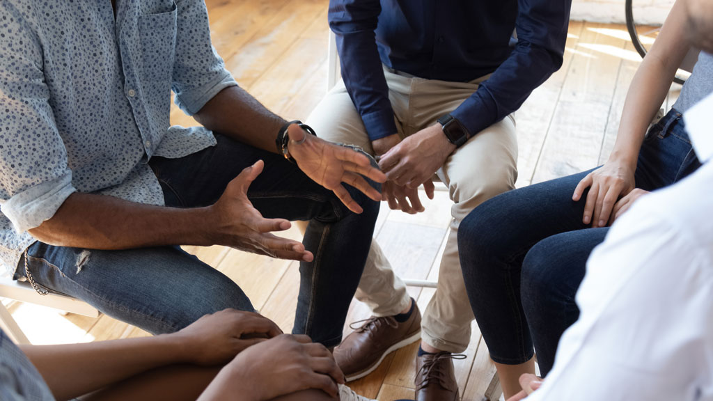 Photo of people seated in a circle and taking part in a discussion with focus on center of group.