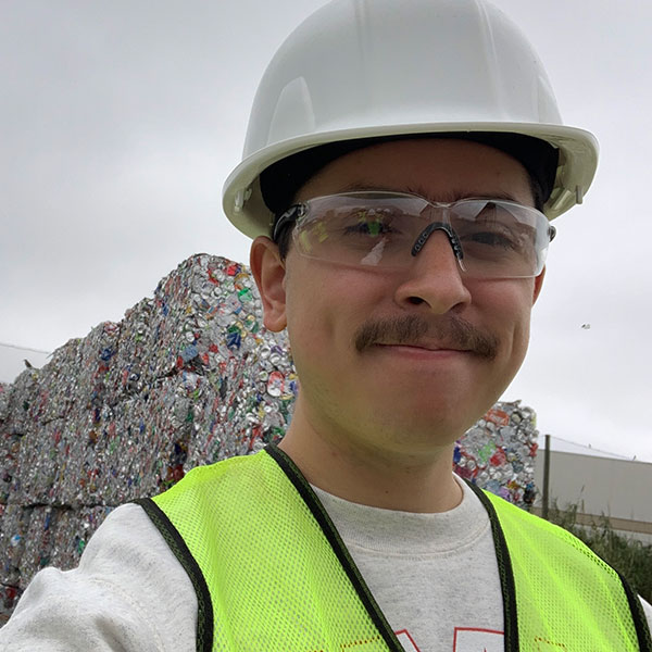 Grant Rodriguez Almani stands in front of a wall of recycling material
