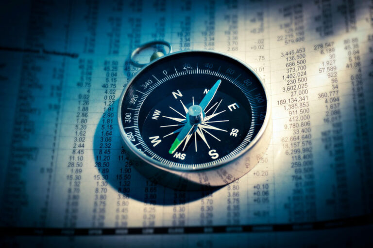 Old-style hand compass in a splash of light against a newspaper with columns of numbers; Photo credit: Alter&Go/AbsolutVision, Unsplash