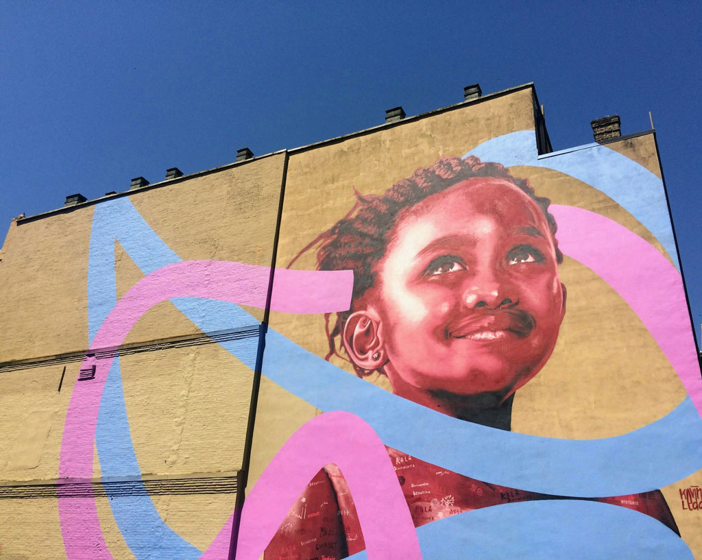 Mural of a young Black child with pink and blue ribbon-like graphics swirling around the image.