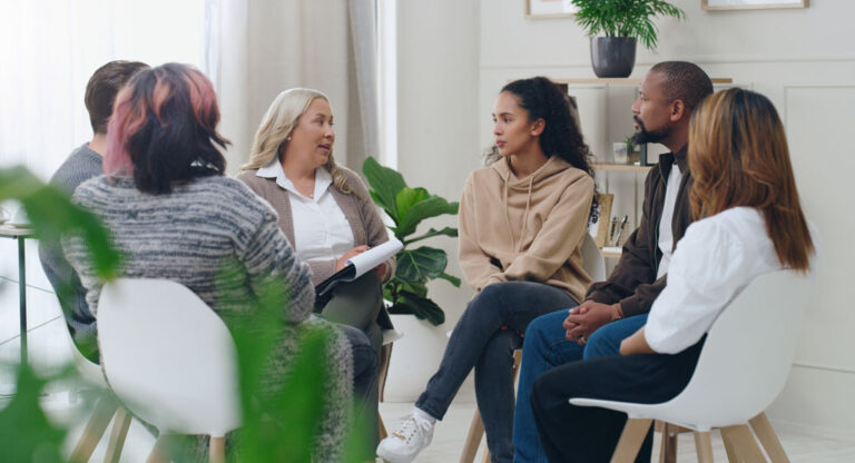 A diverse group of people having a discussion and sitting in a tight circle of chairs.