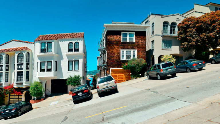 Street hill gradient showing homes built on a slope with cars parked on the deeply slanted street.