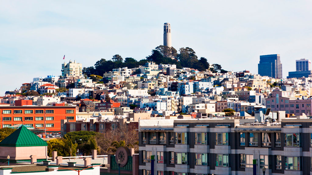 View of Telegraph Hill from below showing buildings and homes rising up to the tower atop the hill.