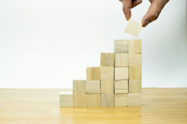 Image showing a hand piling up small square blocks to build a stair structure.